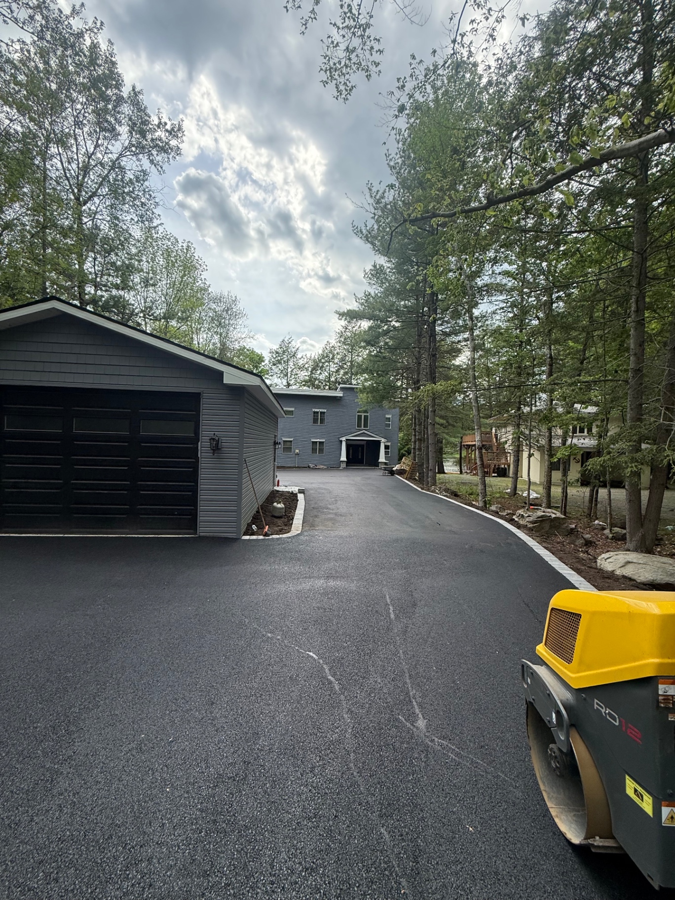 Freshly paved asphalt driveway leading to a navy home in the woods