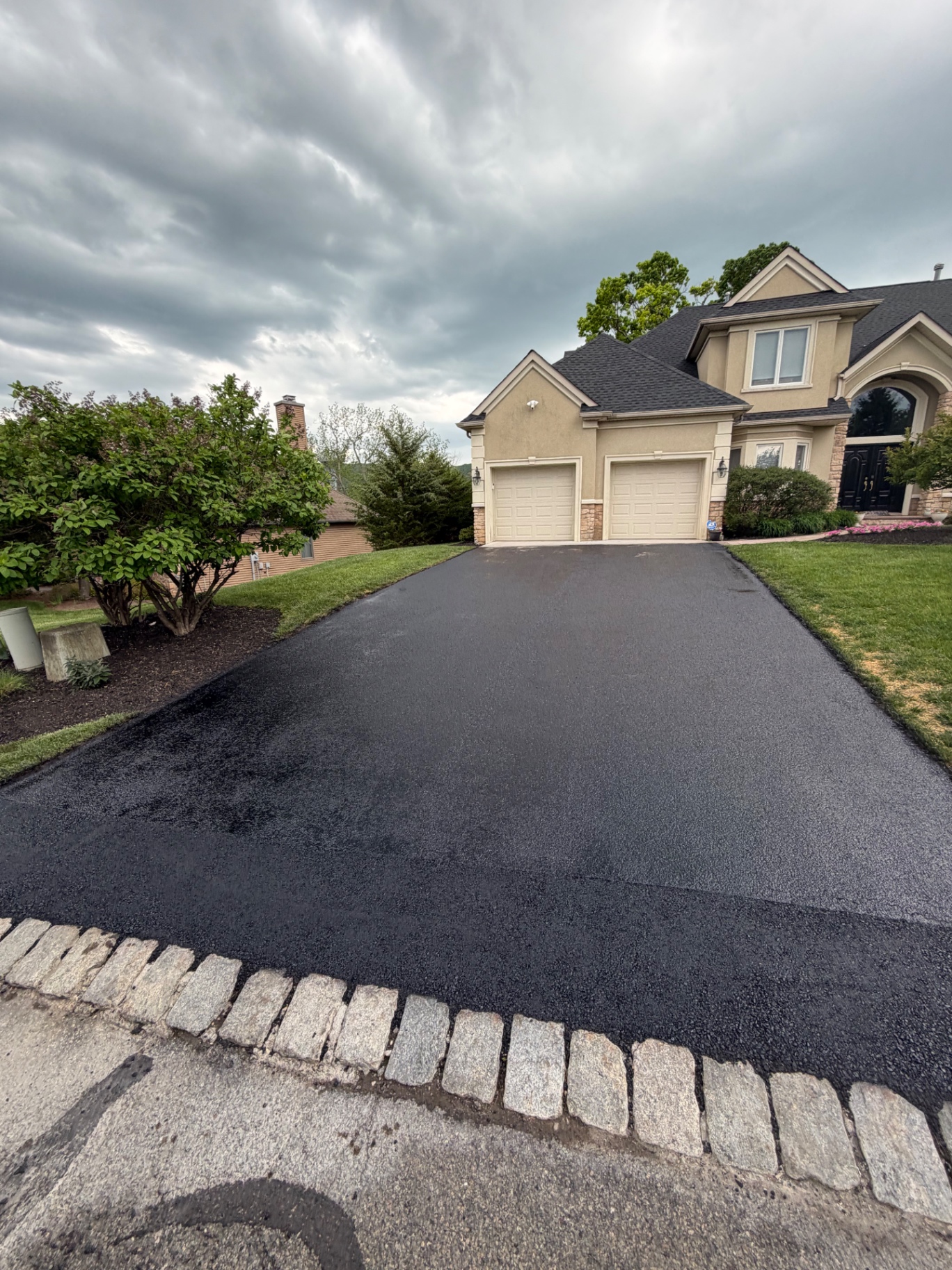 Glossy freshly sealed driveway with cobblestone curb in front of a large home